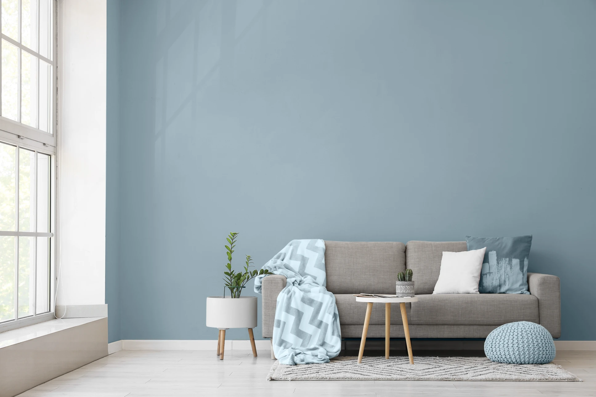 Photographie d'un professionnel de la peinture en action dans un intérieur en cours de rénovation. Le peintre, vêtu de manière professionnelle, applique de la peinture au rouleau sur un mur blanc dans un salon lumineux. La scène montre un chantier bien organisé avec bâches de protection au sol, escabeau, seaux de peinture et outils professionnels. Lumière naturelle par fenêtre. Atmosphère de transformation et de professionnalisme, incarnant les services de peinture intérieure et rénovation de l'entreprise.